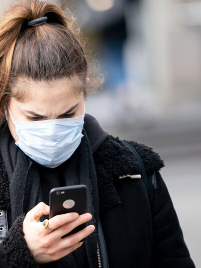 A woman wearing a mask looks at her smartphone.