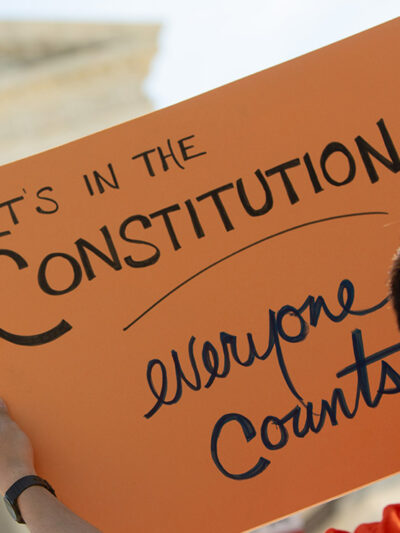 A demonstrator holding a sign with the text "It's in the Constitution: everyone counts" outside the Supreme Court.