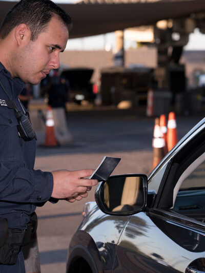 A U.S. Customs and Border Protection checking the identification of someone seated in a car.