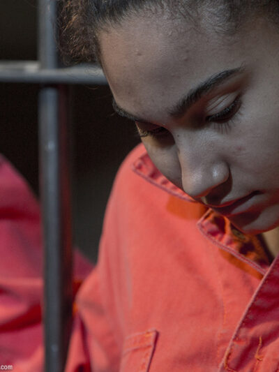 A incarcerated woman standing behind bars.