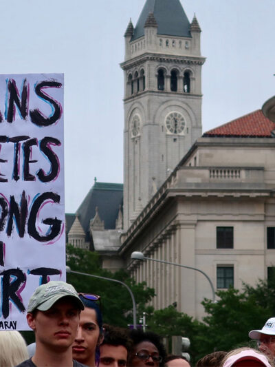 A crowd of marchers with one holding a sign with the text " Trans Athletes Belong in Sport."