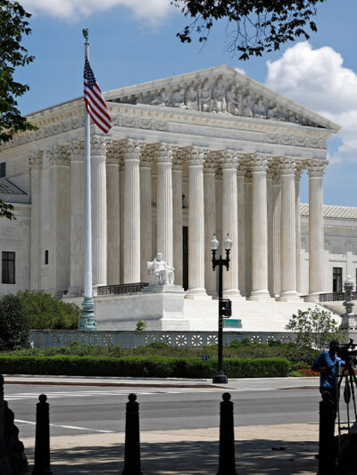 Photo of the American flag on a flag pole and the Supreme Court in Washington, DC.