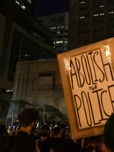 A group of protesters with one holding a sign with the text, "Abolish the Police."