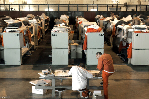 Incarcerated people lying in rows of prison bunk beds.