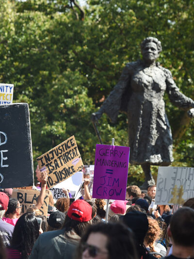 Marchers carry their signs into Lincoln Park with the Mary McLeod Bethune Memorial in the background.
