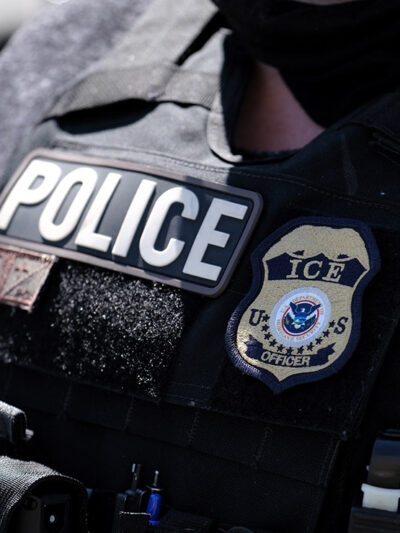 A close up of a police officer wears a "Police" label beside a U.S. ICE (standing for Immigration and Customs Enforcement) badge on his vest.