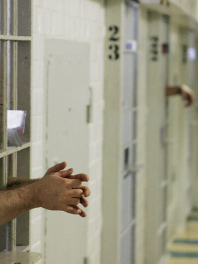 Prisoners reach through the metal bars of their cells.