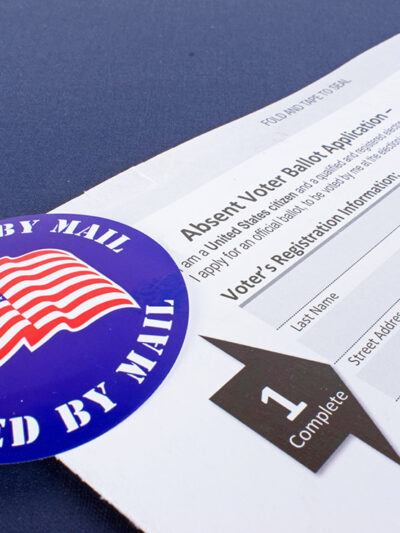 An absentee voter ballot next to a blue "I voted by mail" sticker.