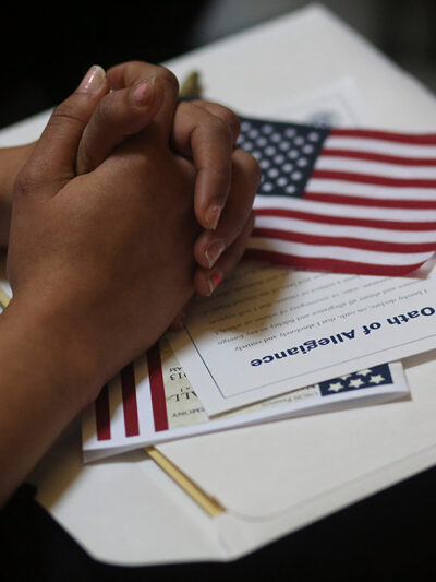 A participant folds her hands of a copy of the Oath of Allegiance and an American flag while listening to speeches during a naturalization ceremony