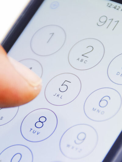 Hand holding smartphone with emergency number 911 on the screen.