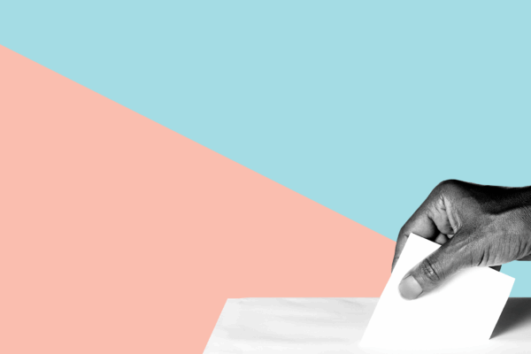 A hand putting a ballot into a ballot box.