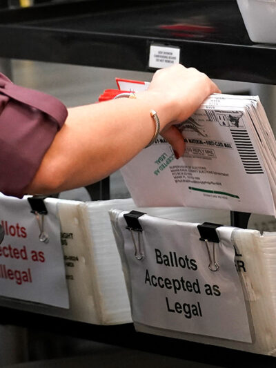 An election worker sorts vote-by-mail ballots in bins.