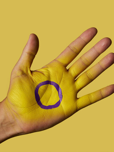 A closeup of the intersex flag painted on the palm of a person's hand.