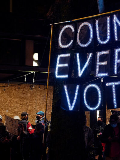 Demonstrators carrying a banner with the text "Count Every Vote" spelled out in LED bulbs.