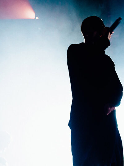 Silhouette of a rapper onstage with bright stage light and smoke in the background.