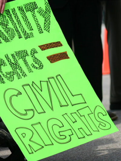 A wheelchair user holding a sign with the text "Disability rights = civil rights."