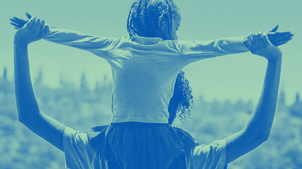 Child sitting on parent's shoulders with arms outstretched.