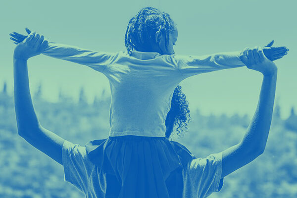 Child sitting on parent's shoulders with arms outstretched.