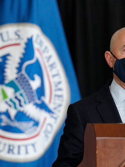 Secretary of Homeland Security Alejandro Mayorkas speaks during news conference with a U.S. Homeland Security flag behind him.