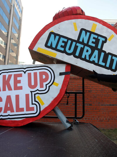 Woman helps to dismantle a large alarm clock display that reads "Net Neutrality Wake Up Call" from the stage after a protest in front of the FCC in Washington, DC.