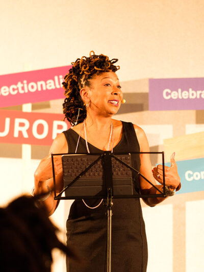 Kimberlé Crenshaw gives presentation at podium with "Intersectionality" and "celebrate differences" sign behind her.