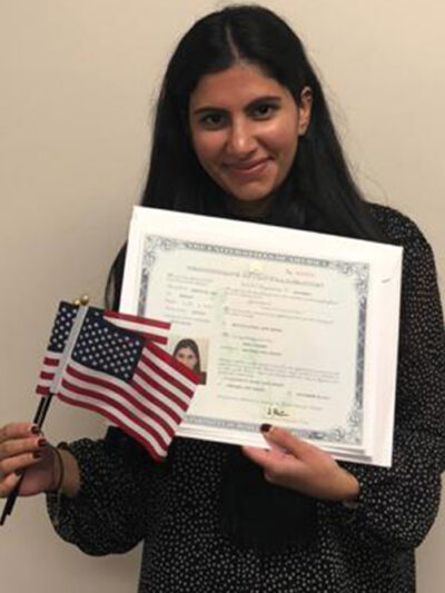 Mira Naseer, a diversity visa recipient, holding her naturalization papers and two American flags.