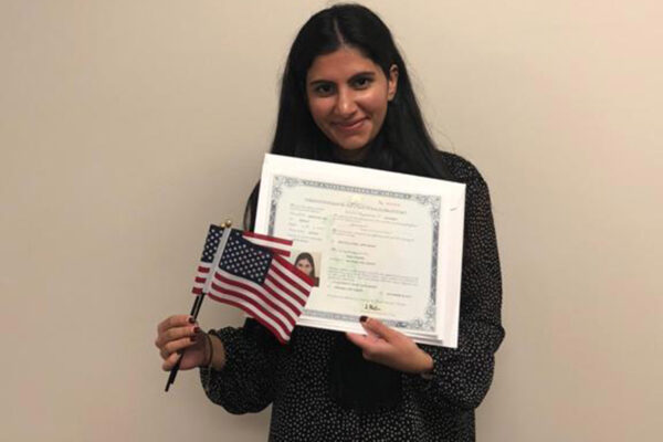 Mira Naseer, a diversity visa recipient, holding her naturalization papers and two American flags.