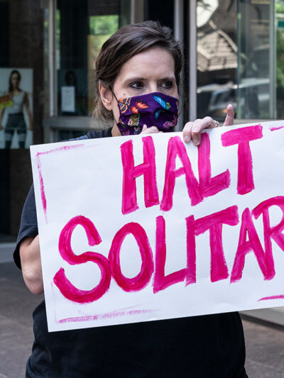 Woman holds sign that reads "halt solitary" as demand to end solitary confinement in prisons