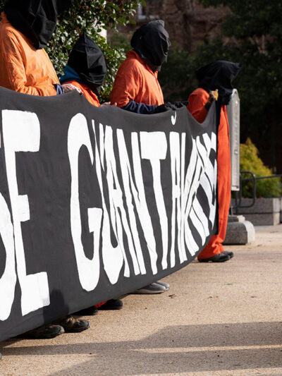 Demonstrators dressed like Guantanamo Bay detainees, hold a banner asking to close Guantanamo.