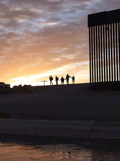 A pair of migrant families at the border wall between the United States and Mexico.