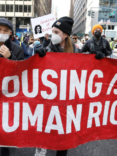 Protesters marching and holding a sign reading Housing Is A Human Right.