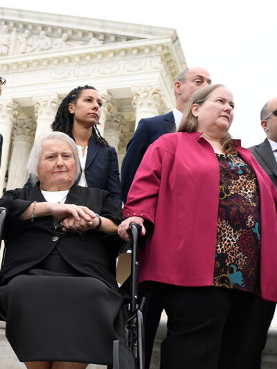 Aimee Stephens, seated, her wife Donna Stephens, in pink, and ACLU attorney Chase Strangio, at the far right listen during a news conference outside the Supreme Court.
