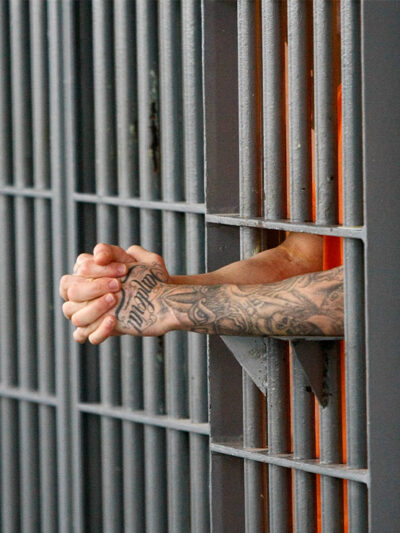 A prisoner holding his extended and clasped hands between the bars of his cell.