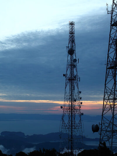 A photo of three cell phone towers in front of a sunset.