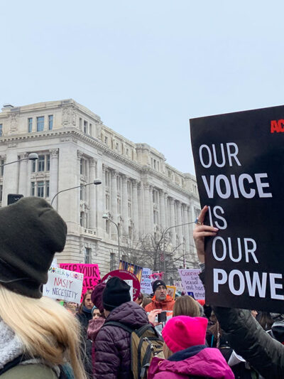 A protestor holding a sign with an ACLU logo that says Our Voice is Our Power.
