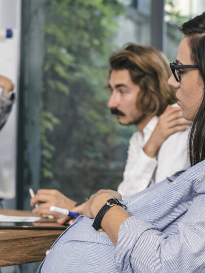 A seated pregnant woman participating in a brainstorming meeting.