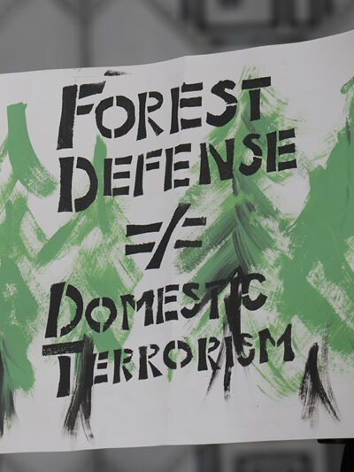 A protester holdng a sign stating "Forest Defense =/ Domestic Terrorism" demands the end of planned construction of Atlanta's proposed police training facility, "Cop City" to save the Weelaunee Forest.