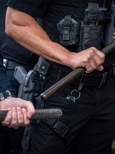 Two cops who are only visible from the chest to waist and are holding batons.