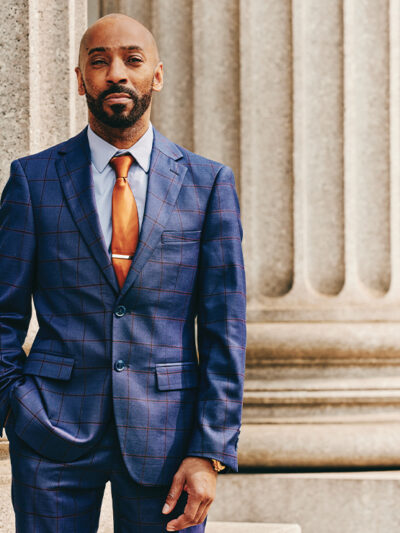 Daudi Justin standing in front of a marble column with his left hand in his pant pocket.