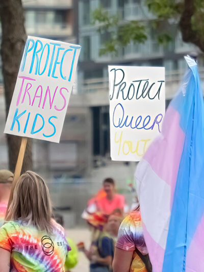 A person holding a sign with the text: Protect Trans Kids, during the pride parade.