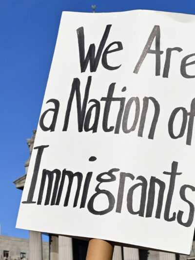 Two signs are held up during the May Day March In Manhattan, New York on May 1, 2025. The largest of the signs is in the foreground and reads"We Are a Nation of Immigrants," while the smaller in the background reads, " WE ARE ALL (EXCEPT NATIVE...