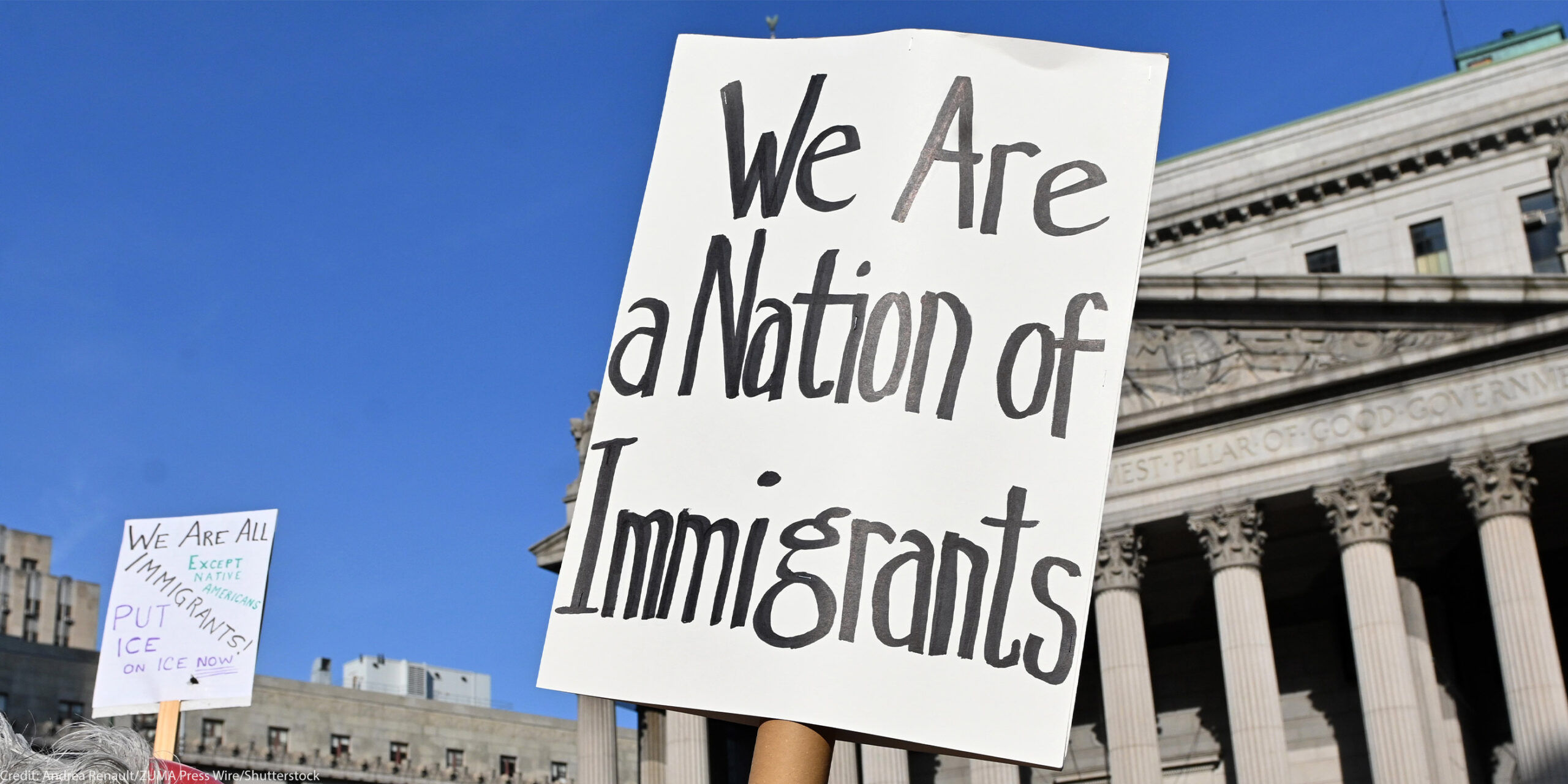 Two signs are held up during the May Day March In Manhattan, New York on May 1, 2025. The largest of the signs is in the foreground and reads"We Are a Nation of Immigrants," while the smaller in the background reads, " WE ARE ALL (EXCEPT NATIVE...