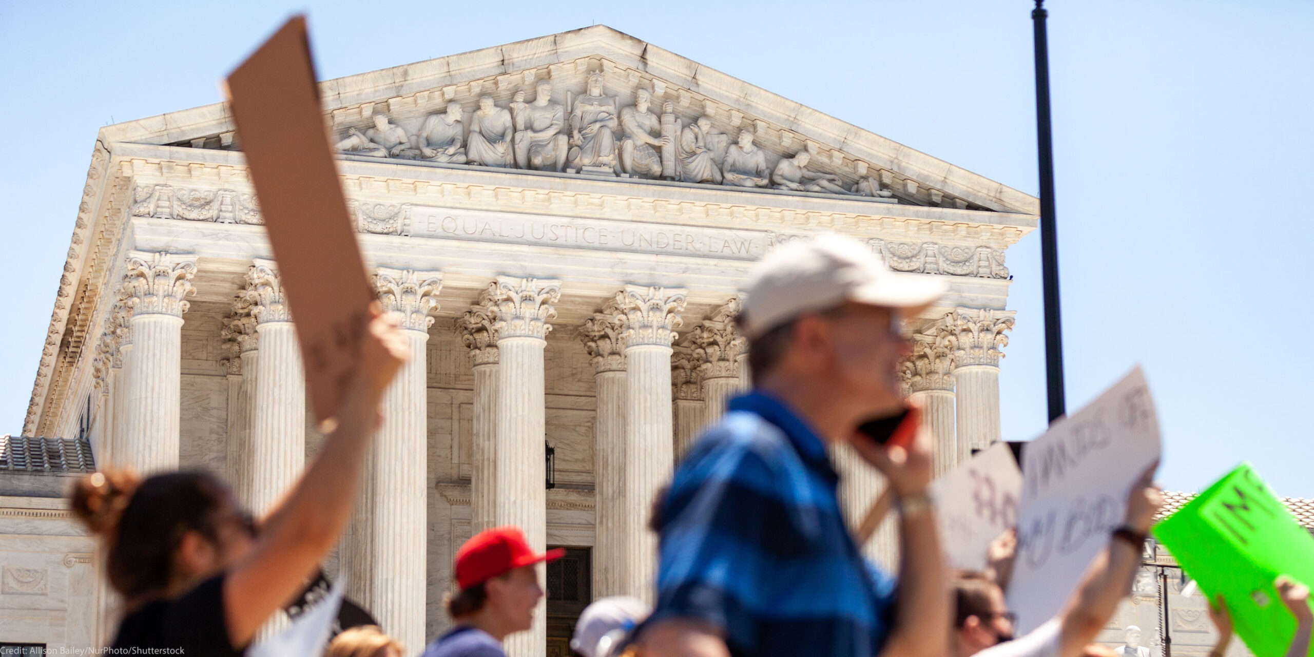 Pro-choice demonstrators (whose faces and signs are blurred) march in front of the Supreme Court and the statement on its facade, "Equal justice under law".