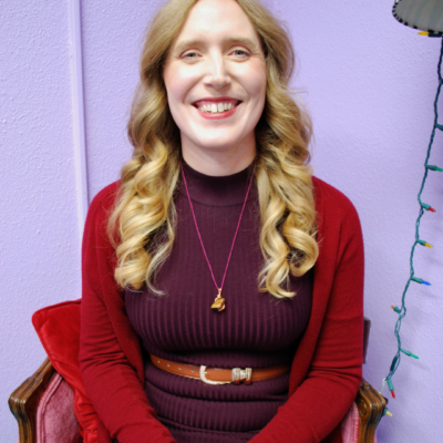 Female presenting with purple background and red sweater over a maroon top