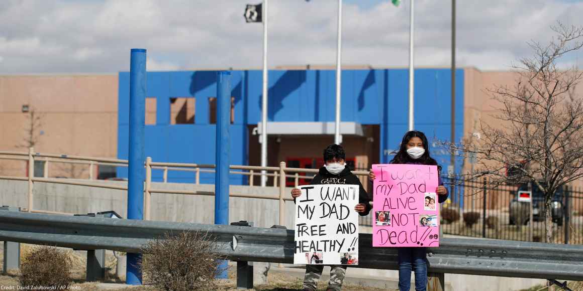 Two children wear masks and hold signs that read "I want my dad free and healthy" and "I want my dad alive not dead!!" as part of a protest calling for the release of detained immigrants in front of the GEO Detention Center in Aurora, Colorado.