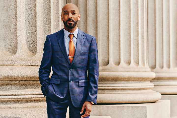 Daudi Justin standing in front of a marble column with his left hand in his pant pocket.