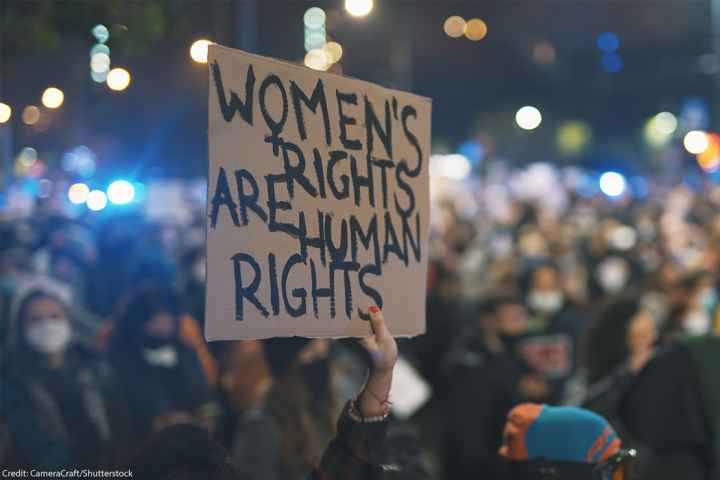 A sign reading "WOMEN'S RIGHTS ARE HUMAN RIGHTS" is held high by women's rights advocates.