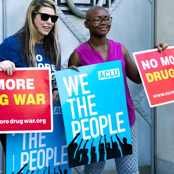 Two protestors holding 'No More Drug War' and ACLU's 'We the People' posters at a protest in front of the Justice Department.