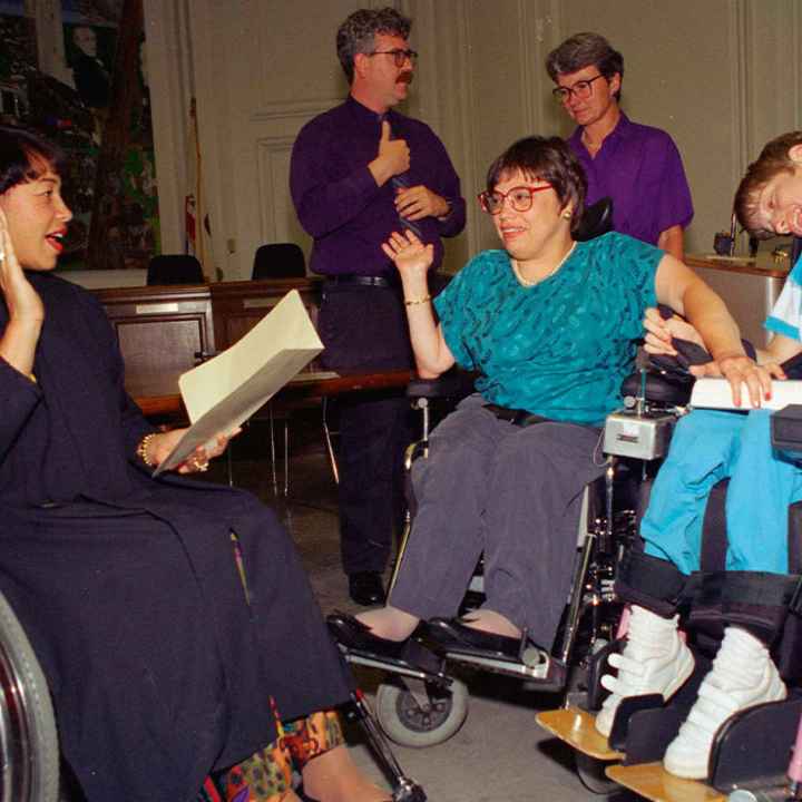 Judy Heumann, center wheelchair, is sworn in as U.S. Assistant Secretary for Special Education and Rehabilitative Service by Judge Gail Bereola, left, on June 29, 1993. Standing at left is Berkeley Mayor Loni Hancock with sign language interpreter...