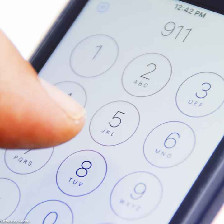 Hand holding smartphone with emergency number 911 on the screen.